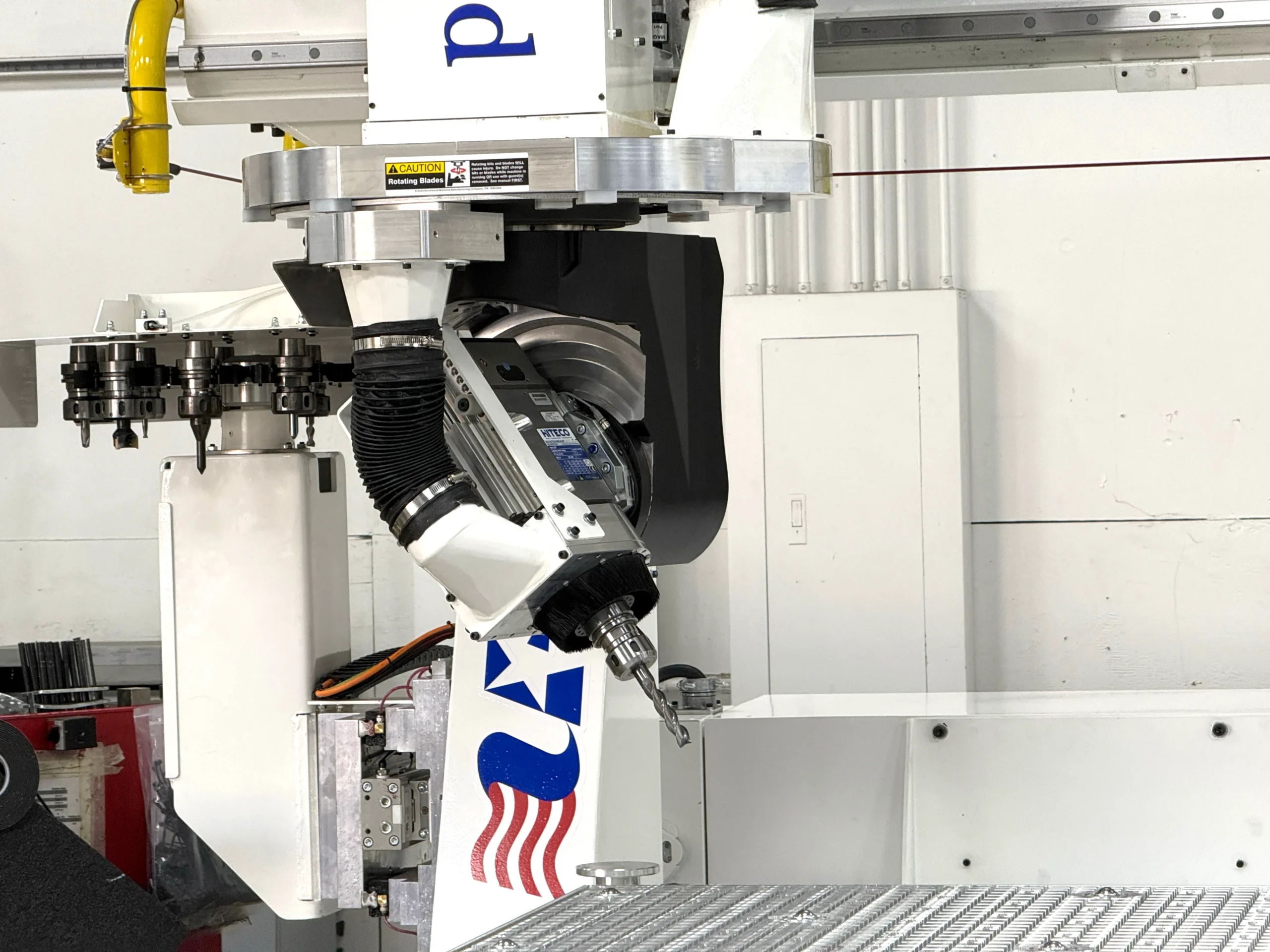 Close-up of a 5-axis CNC machining head on a Northwood machine, showing an angled spindle with a drill bit attached, a tool changer rack with multiple tool holders on the left, and the Northwood star-and-wave logo on the machine body.